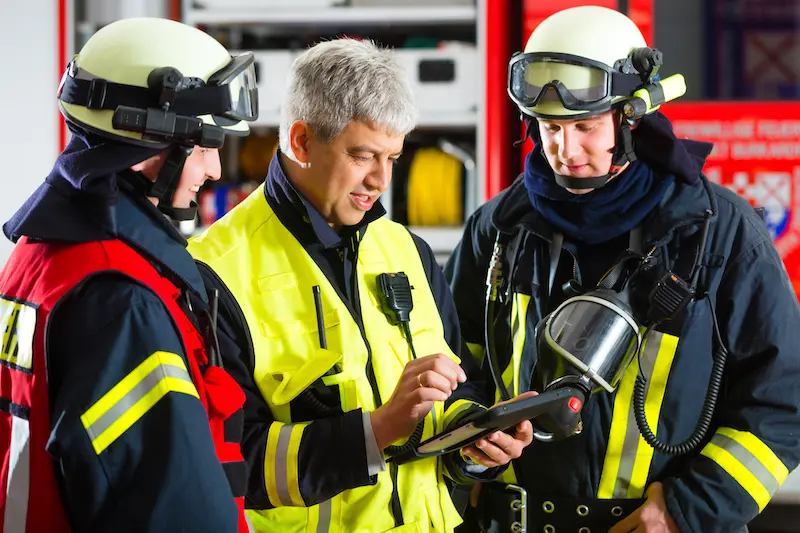 Einsatzkräfte besprechen während eines Notfalls anhand einer digitalen Karte auf einem Tablet die Katastrophenbekämpfung – Beispiel für den Einsatz von GIS in der Katastrophenhilfe.