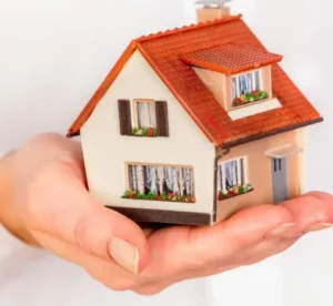 foto van een hand die een miniatuur huis vast houdt.